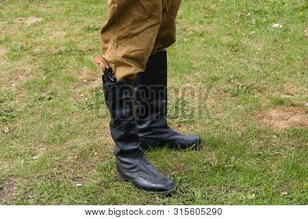 The Legs Of A Soldier In Black Leather Boots On The Lawn