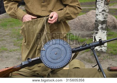 A Soldier Packs A Backpack In Front Of A Wwii Machine Gun.