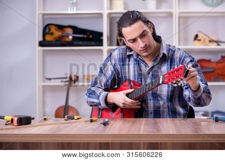 Young handsome repairman repairing guitar