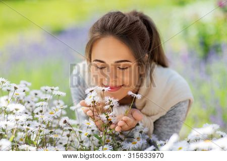 gardening and people concept - close up of happy young woman smelling chamomile flowers at summer garden