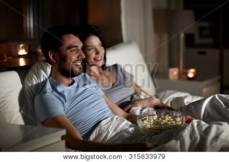 people, family and leisure concept - couple with popcorn watching tv at night at home