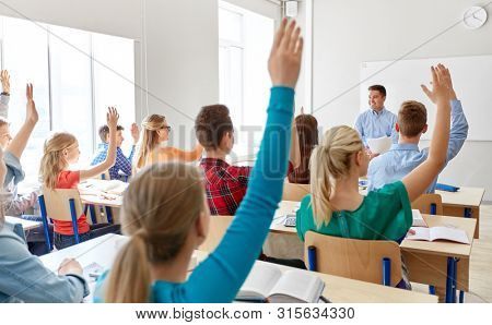 education, learning and people concept - male teacher and group of high school students raising hands in classroom