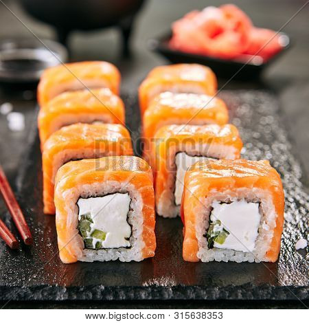 Beautiful Philadelphia Sushi Rolls Set with Salmon and Cream Cheese and Cuccumber on Black Slate Plate Close Up. Uramaki, Nori Maki or Futomaki Sushi with Trout Fillets, Soy Sauce and Wasabi