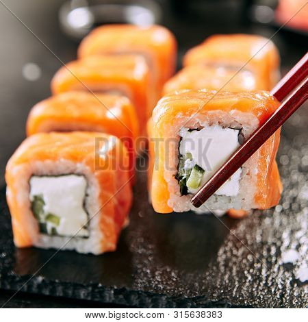Beautiful Philadelphia Sushi Rolls Set with Salmon and Cream Cheese and Cuccumber on Black Slate Plate Close Up. Uramaki, Nori Maki or Futomaki Sushi with Trout Fillets, Soy Sauce and Wasabi