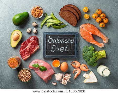 Balanced Diet - Healthy Food On Gray Stone Background. Various Food Ingredients And Chalkboard With 