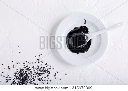 Black Tahini Sauce And Black Sesame Seeds On White Background. Natural Paste Made From Sesame Seeds.
