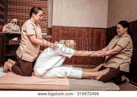 Two Masseuses Stratching Back Of Their Client.