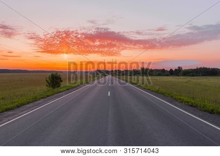 Direct Asphalt Road In The Middle Of A Wheat Field Illuminated By A Beautiful Sunrise