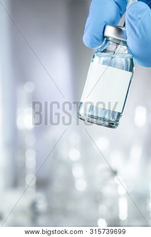Healthcare concept with a hand in blue medical gloves holding a vaccine vial with blue liquid and black white label