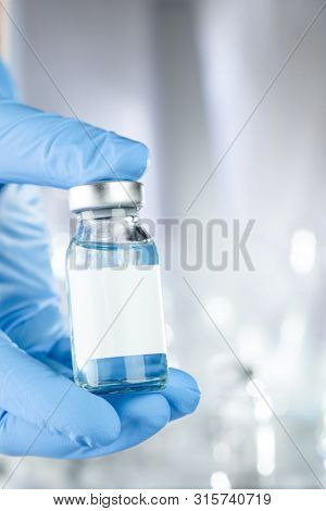 Healthcare concept with a hand in blue medical gloves holding a vaccine vial with blue liquid and black white label