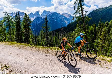 Cycling woman and man riding on bikes in Dolomites mountains andscape. Couple cycling MTB enduro trail track. Outdoor sport activity.