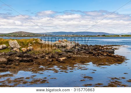 Bay With Low Tide, Seaweeds, Boat And Mountains In Carraroe