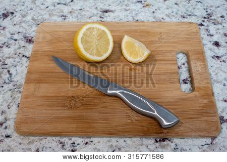 A Cut Lemon On A Wooden Cutting Board With A Knife, Ready For A Drink.