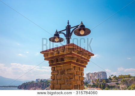 Antique Lantern On A Brick Collar. Brick Collon Against The Background Of Blue Sky And The City Whic