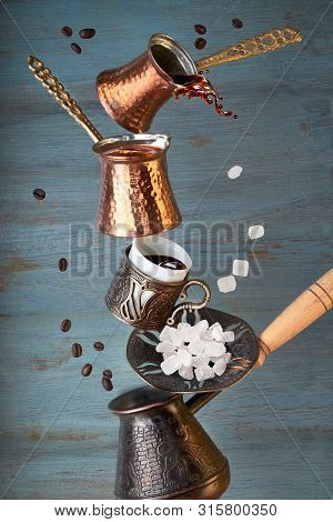 Balancing Pyramid Of Jezves, Turkish Coffee Pots And Cups On Dark Wooden Background With Coffee Bean