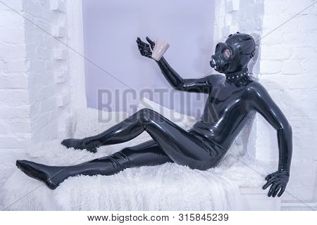 Morning Cup Of Tea Breakfast. Fetish Male In Rubber Black Suit At White Windowsill.
