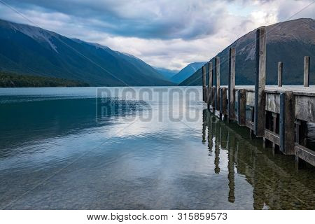 A View Down The Side Of A Wooden Jetty Of The Incredibly Beautiful Rotoiti Lake Surrounded By Mounta