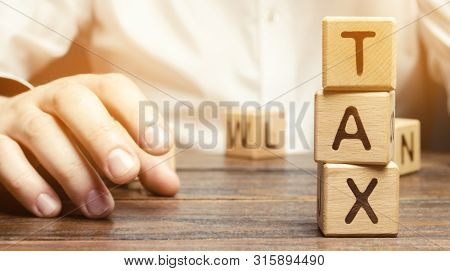 Wooden Blocks With The Word Tax And A Businessman Sitting At The Table. Making The Right Decision. T