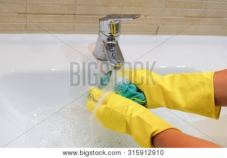 Woman In Yellow Rubber Gloves Holding And Cleaning A Green Rag. Housewife Working At Home. White Sin