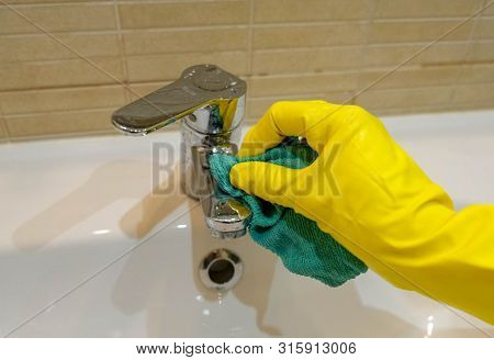 Woman In Yellow Rubber Gloves Cleaning And Polishing A Water Tap. Housewife Holding A Rag. White Sin