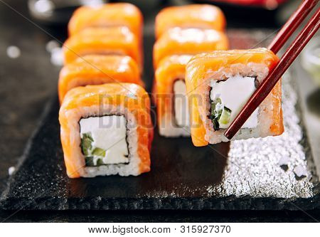 Beautiful Philadelphia Sushi Rolls Set with Salmon and Cream Cheese and Cuccumber on Black Slate Plate Close Up. Uramaki, Nori Maki or Futomaki Sushi with Trout Fillets, Soy Sauce and Wasabi