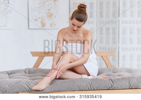 Cute Caucasian Woman In White Towel Applying Cream On Her Skin Before Spa Procedure On The White Sal