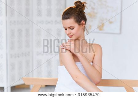Cute Caucasian Woman In White Towel Applying Cream On Her Skin Before Spa Procedure On The White Sal