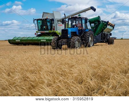VILLAGE DECABRIST, SARTOV REGION, RUSSIA - AUGUST 03, 2019: Combine harvesters and tractors in the field for harvesting wheat