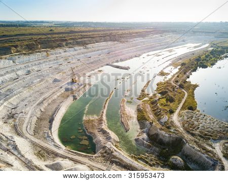 Opencast mining quarry with machinery at work - Aerial view. Industrial Extraction of lime, chalk, calx, caol. View from above