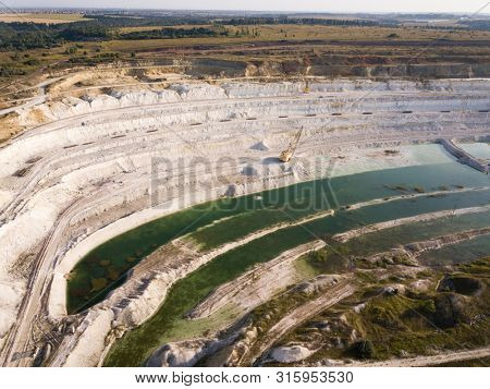 Opencast mining quarry with machinery at work - Aerial view. Industrial Extraction of lime, chalk, calx, caol. View from above