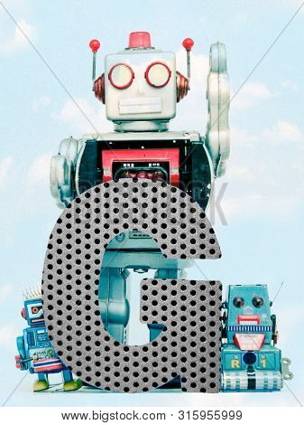 retro robots holding a big  metal letter G with blue sky and clouds