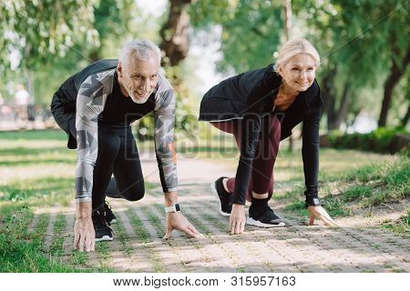Cheerful Mature Runners Standing In Start Positing On Pavement In Park