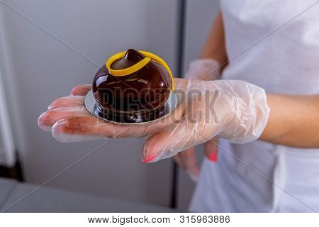 The Pastry Chef In The Kitchen Glazes Pastries. Cook Demonstrates A Finished Chocolate Glazed Cake.