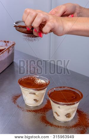 Pastry Chef In The Kitchen Makes Tiramisu With Raspberries. Cook Sprinkles Cocoa On A Prepared Desse