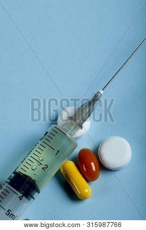 A Lot Of Bright Colored Medicine Pills And Syringe On A Blue Background. Cropped Shot, Vertical, Top