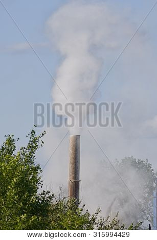 Smoke, Air Emissions From An Industrial Pipe Against Green Trees. Pollution Of The Environmen.