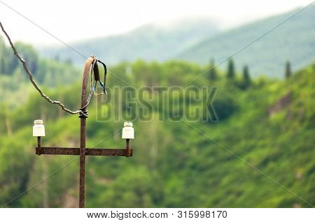 Old Rusty Electric Power Riser Pole, Wires With Electrical Tape, Insulators On Misty Wooded Mountain