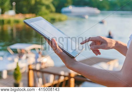 A Finger In Front Of A Tablet Screen In The Hands Of A Girl. Against The Background Of Water With A