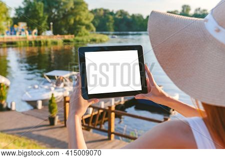 Mock Up Tablet In The Hands Of A Girl In A Big Hat. Against The Background Of A Wooden Embankment Wi