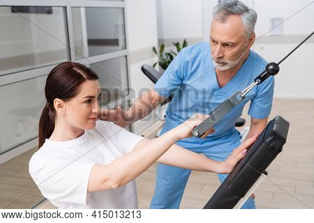 Mature Rehabilitologist Assisting Woman Training In Rehabilitation Center.