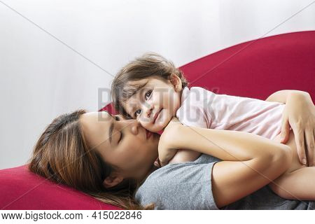 Mother Day Concept.young Mother Kiss Mixed Race Daughter Having Fun While Lying Down Together On Red