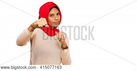 Young african american woman wearing traditional islamic hijab scarf punching fist to fight, aggressive and angry attack, threat and violence 