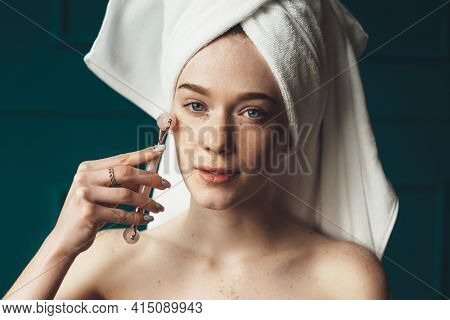 Caucasian Ginger Woman With Freckles Is Massaging Her Face With A Derma Roller Looking At Camera Wit