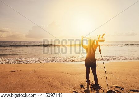 Woman Hold Surfboard Standing At Tropical Sunset Beach Background. Summer Vacation And Sport Adventr