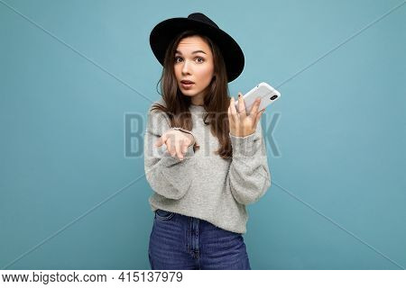 Beautiful Young Asking Dissatisfied Brunette Woman Wearing Black Hat And Grey Sweater Holding Smartp