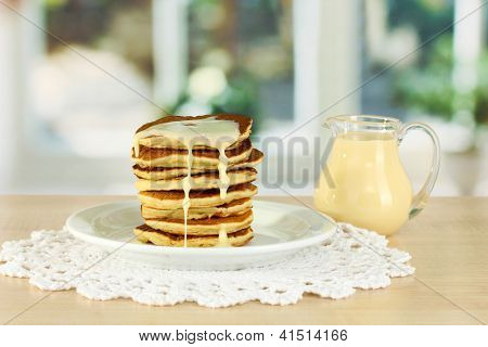หวาน pancakes บนแผ่นกับนมข้นบนโต๊ะในห้องครัว