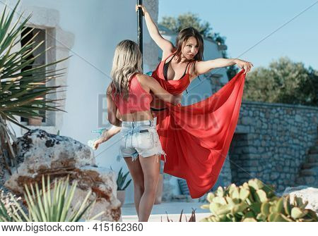 Instructor Helping Young Pole Dancer In A Dress To Take A Pose On A Portable Platform Against The Ga