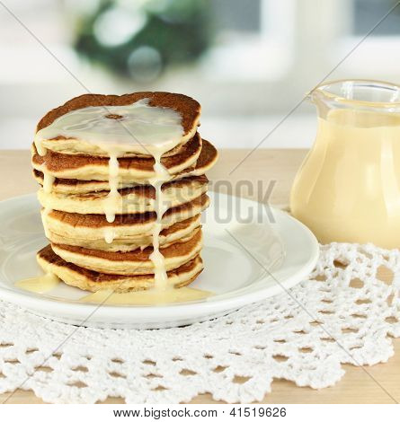 หวาน pancakes บนแผ่นกับนมข้นบนโต๊ะในห้องครัว