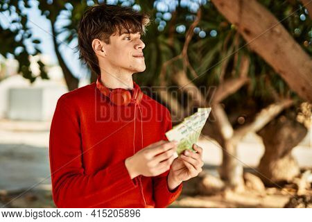 Young hispanic man using headphones counting argentinian pesos at the city
