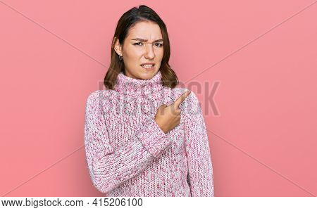 Young caucasian girl wearing wool winter sweater pointing aside worried and nervous with forefinger, concerned and surprised expression 